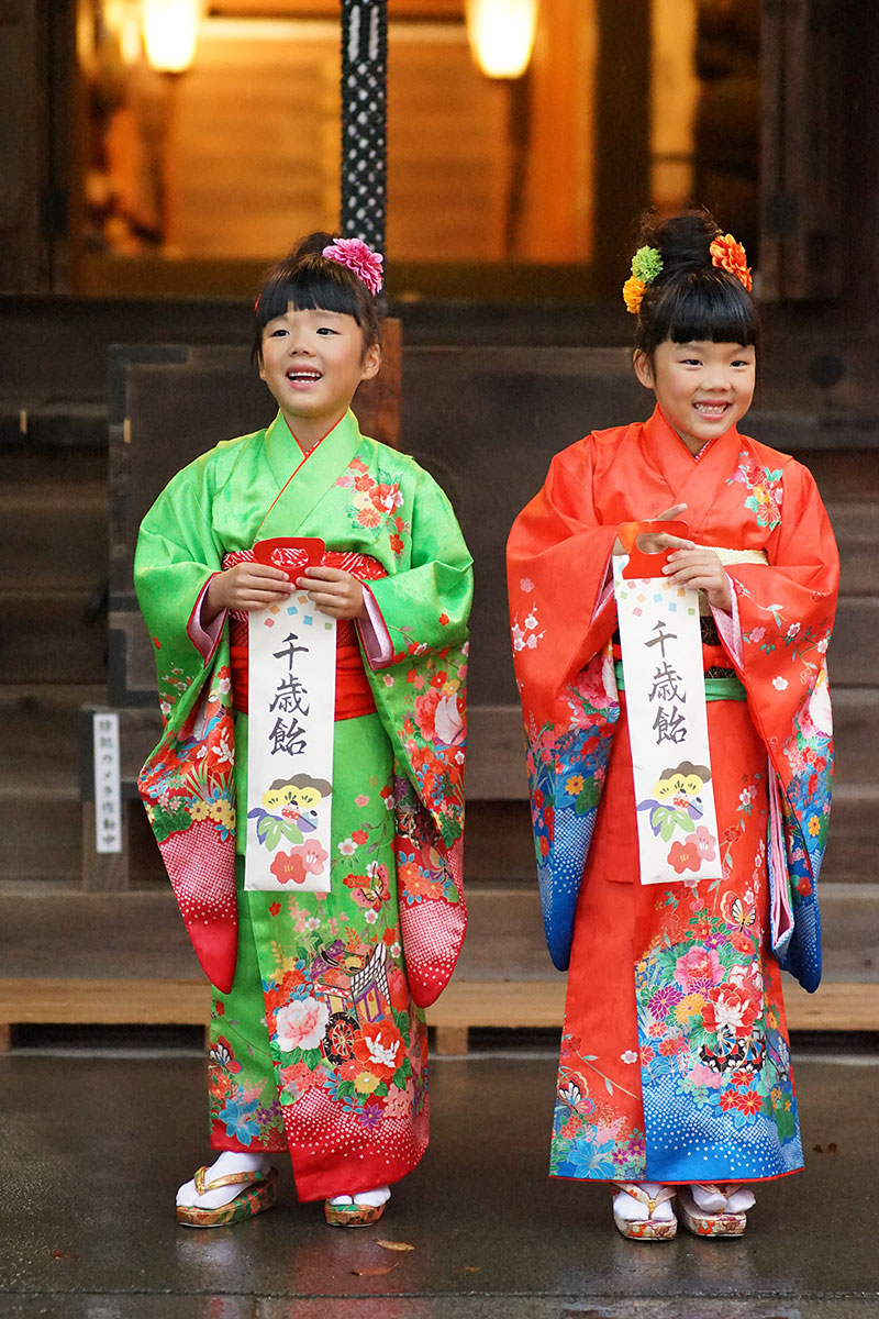 神社で千歳飴を手にする七五三の姉妹